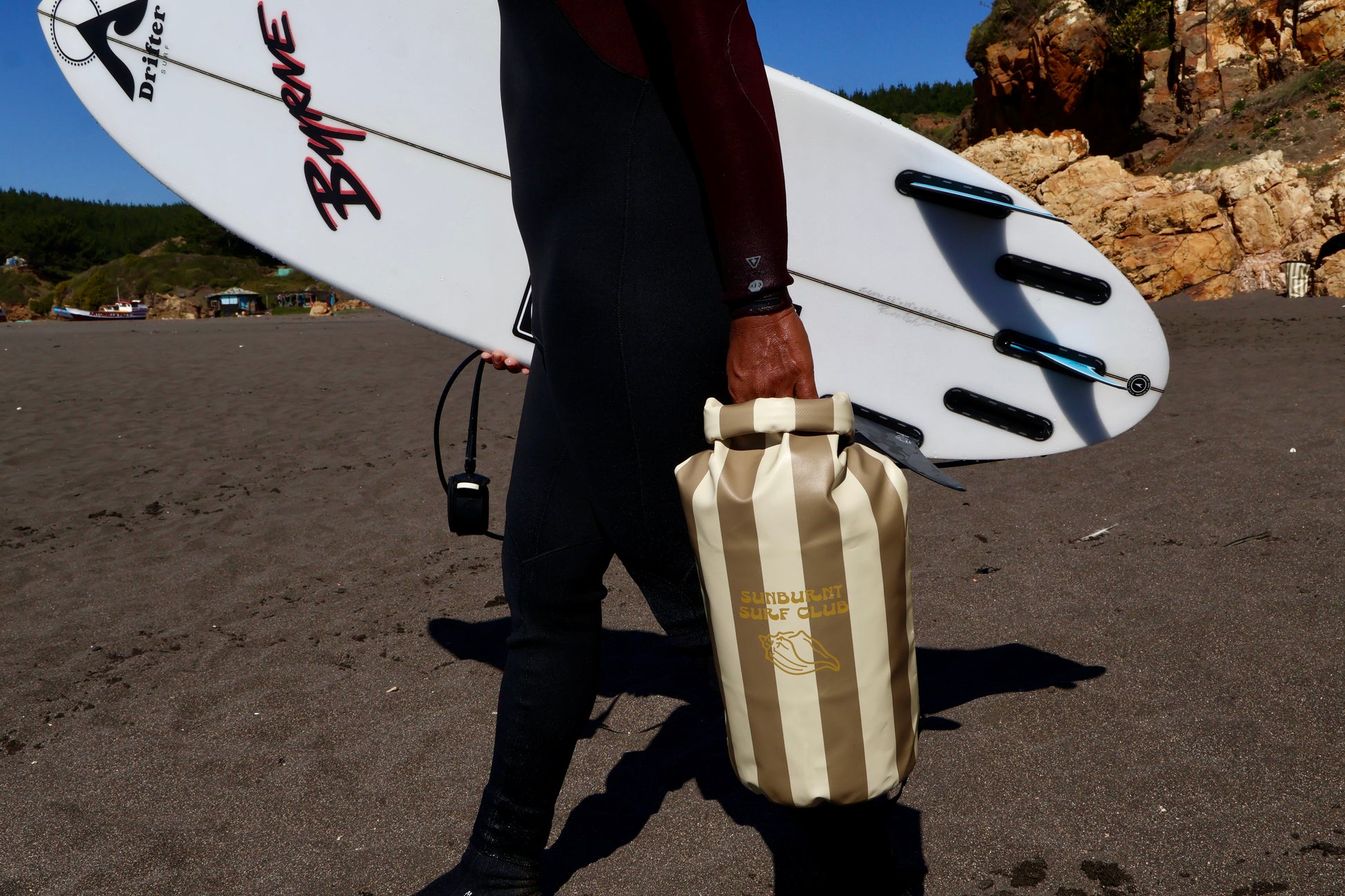 surfer boy holding a striped dry bag nd surfboard
